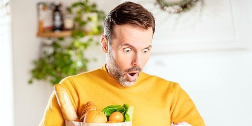 Man looking shocked at food prices on supermarket receipt